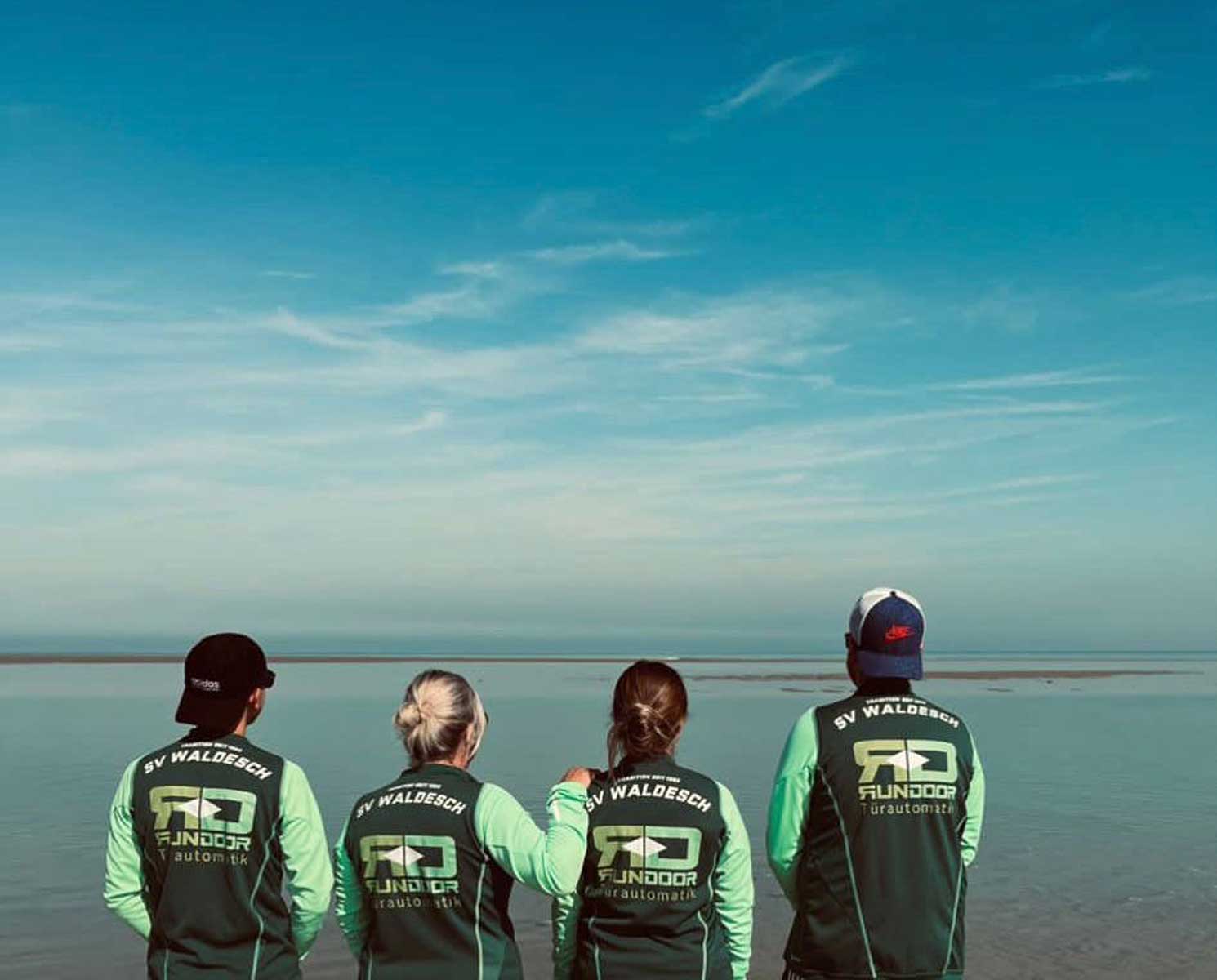 Trikot auf Tour - Zwei Frauen und zwei Männer mit Blick auf das Meer in einer Bucht