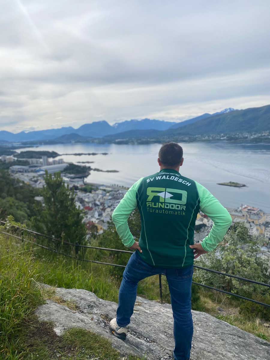 Trikot auf Tour - Mann mit Blick auf einen großen See inmitten einer Berglandschaft