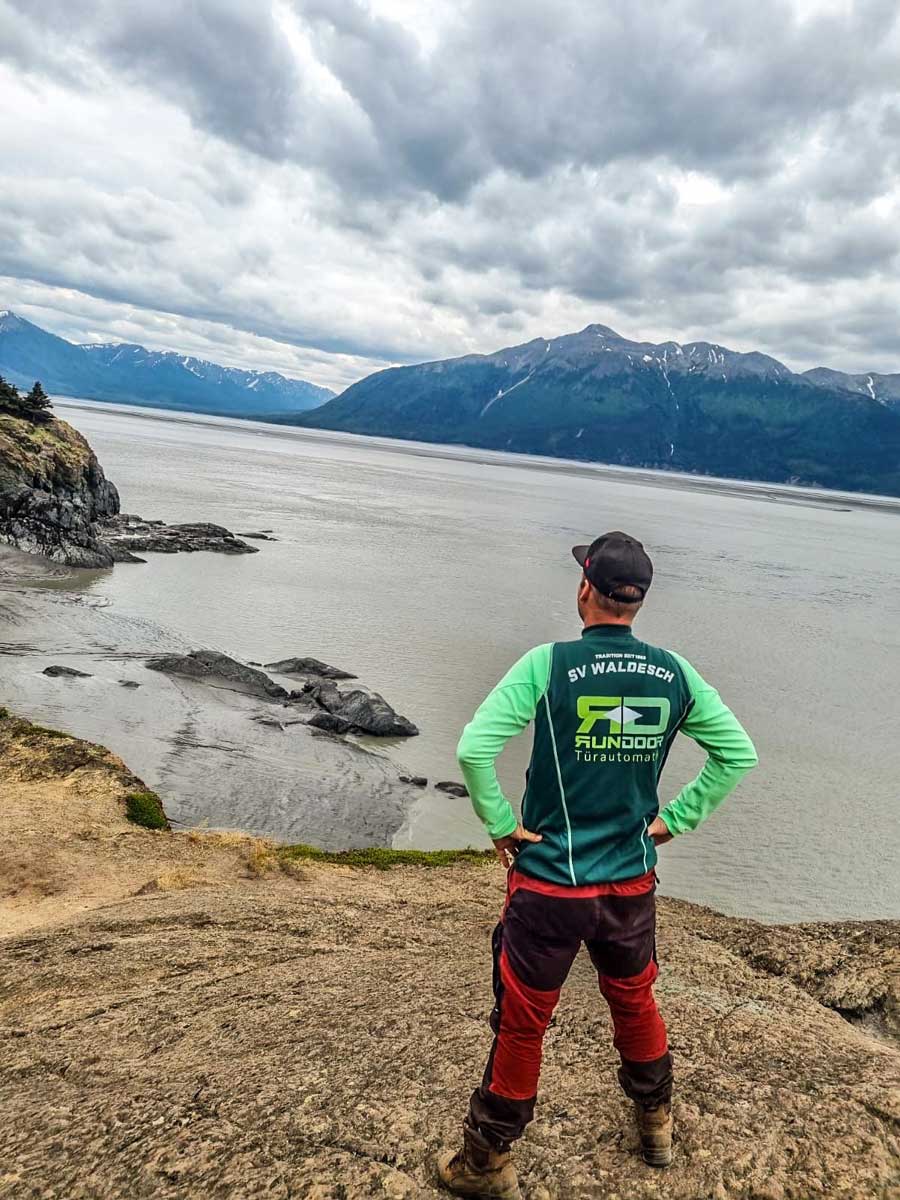 Trikot auf Tour - Mann mit Basecap blickt auf einen Gletschersee oder Fjord
